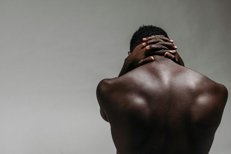 The glowing dark skin on the back of a person with hands clasped behind the neck, set against a gray background