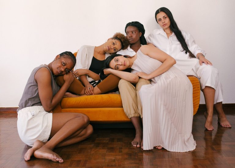 A group of five multiethnic women lounging on a couch