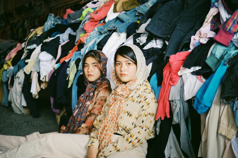 Two Asian Women Sitting in Front of Heaps of Clothing